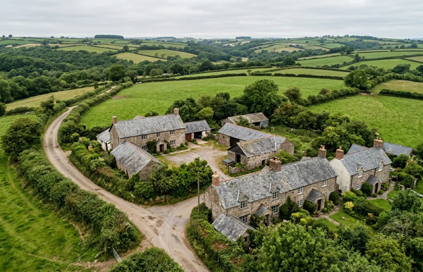 Aerial view over a rural Devon lane with a hedged farmhouse and cottage cluster and no obvious hardstanding
